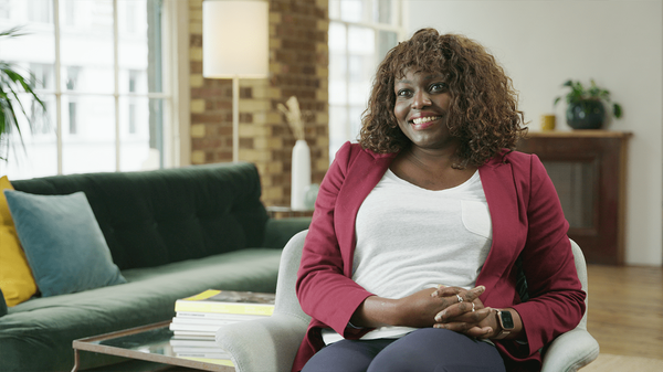 Managing creativity and AI, featuring Anu Adegbola, founder and CMO, PPC Live U.K., who has dark skin and shoulder-length curly red hair, and wears a red blazer, a white scoop-neck top, and gray pants.